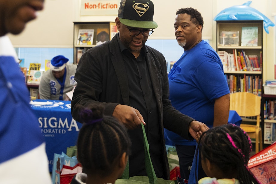 caption: Rogers Greene, center, a family support worker at Dunlap Elementary School, gives bags of gifts to students on Friday, Dec. 20, 2024, at Dunlap Elementary School in Seattle.